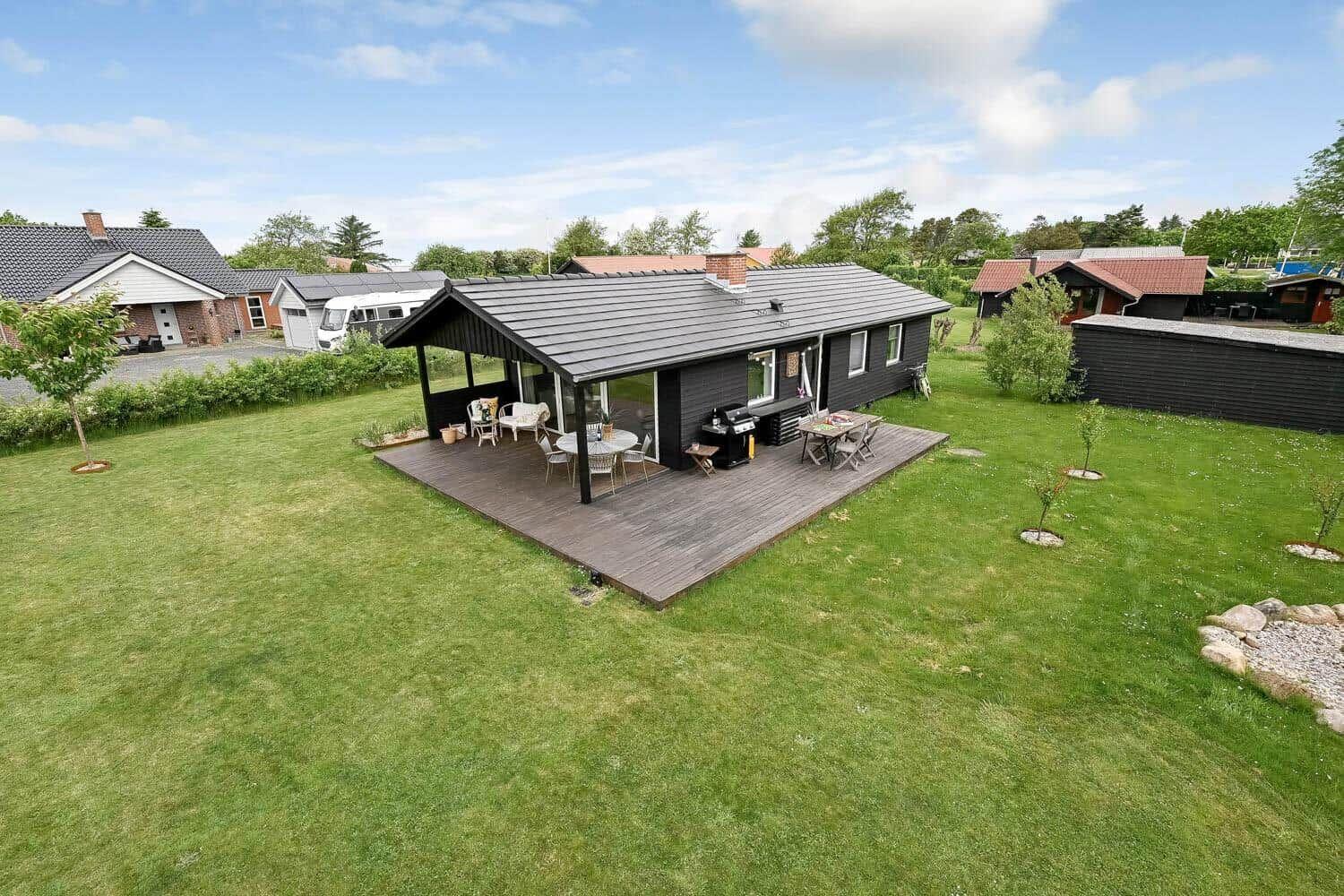 Terrasse mit Sitzgelegenheiten, Tisch und Stühlen unter Laterne. Holzdeck und Glaswand.