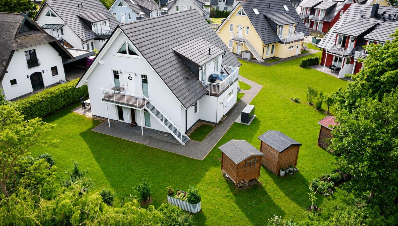 Weißes Haus mit Balkon und Garten. Holzschuppen und grüne Flächen.