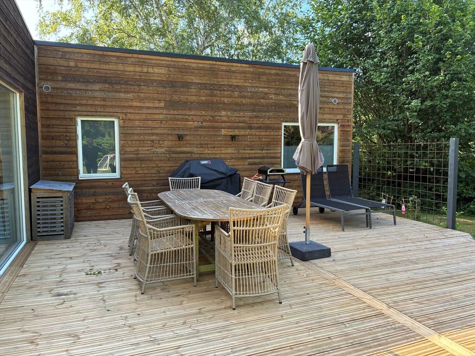 Holzveranda mit zwei Rattanstühlen und Blumenkübeln vor einem Holzhaus.