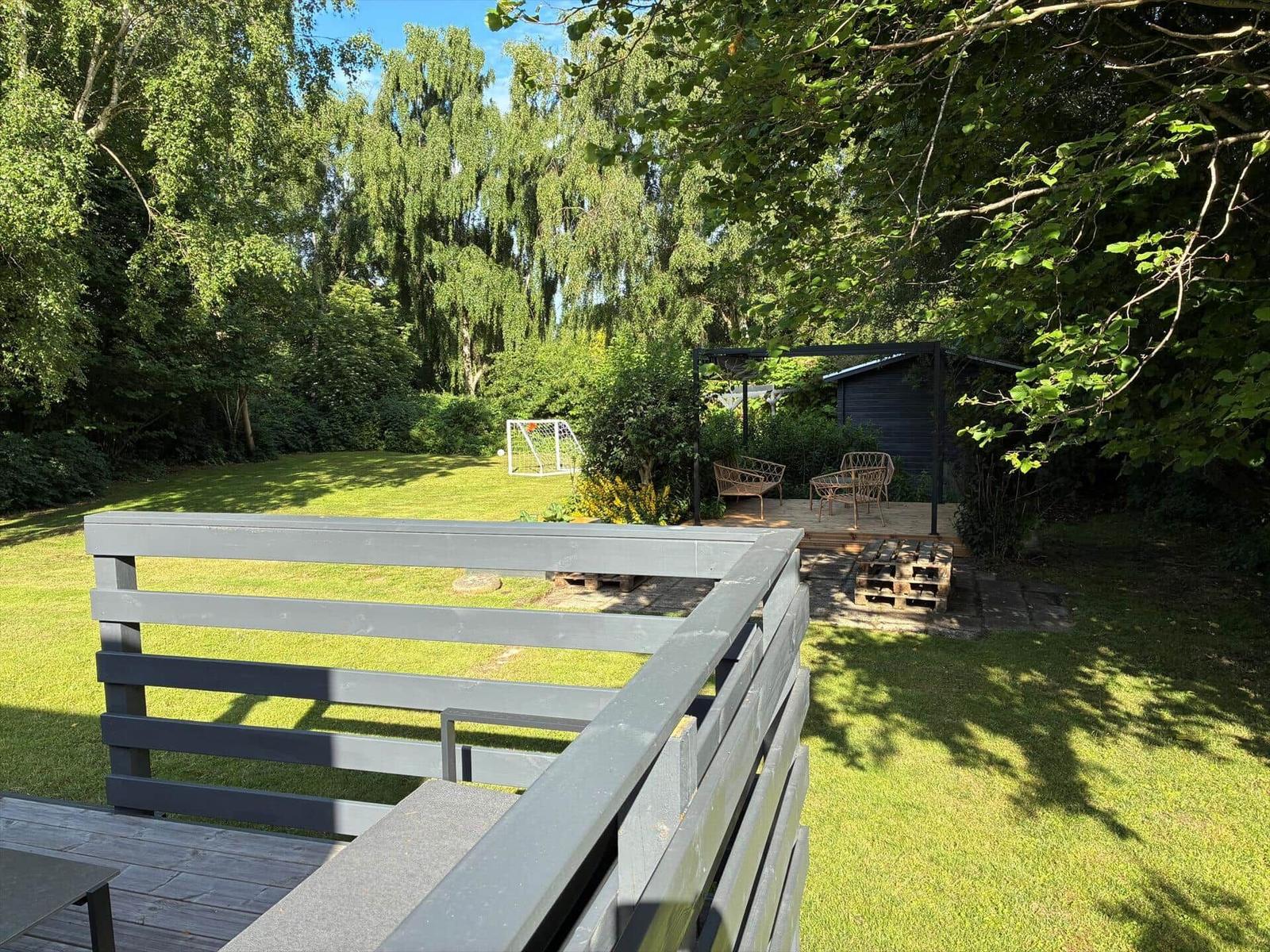 Holzhaus mit Terrasse, zwei Stühlen und Fenstern. Umgeben von Bäumen und Gras.