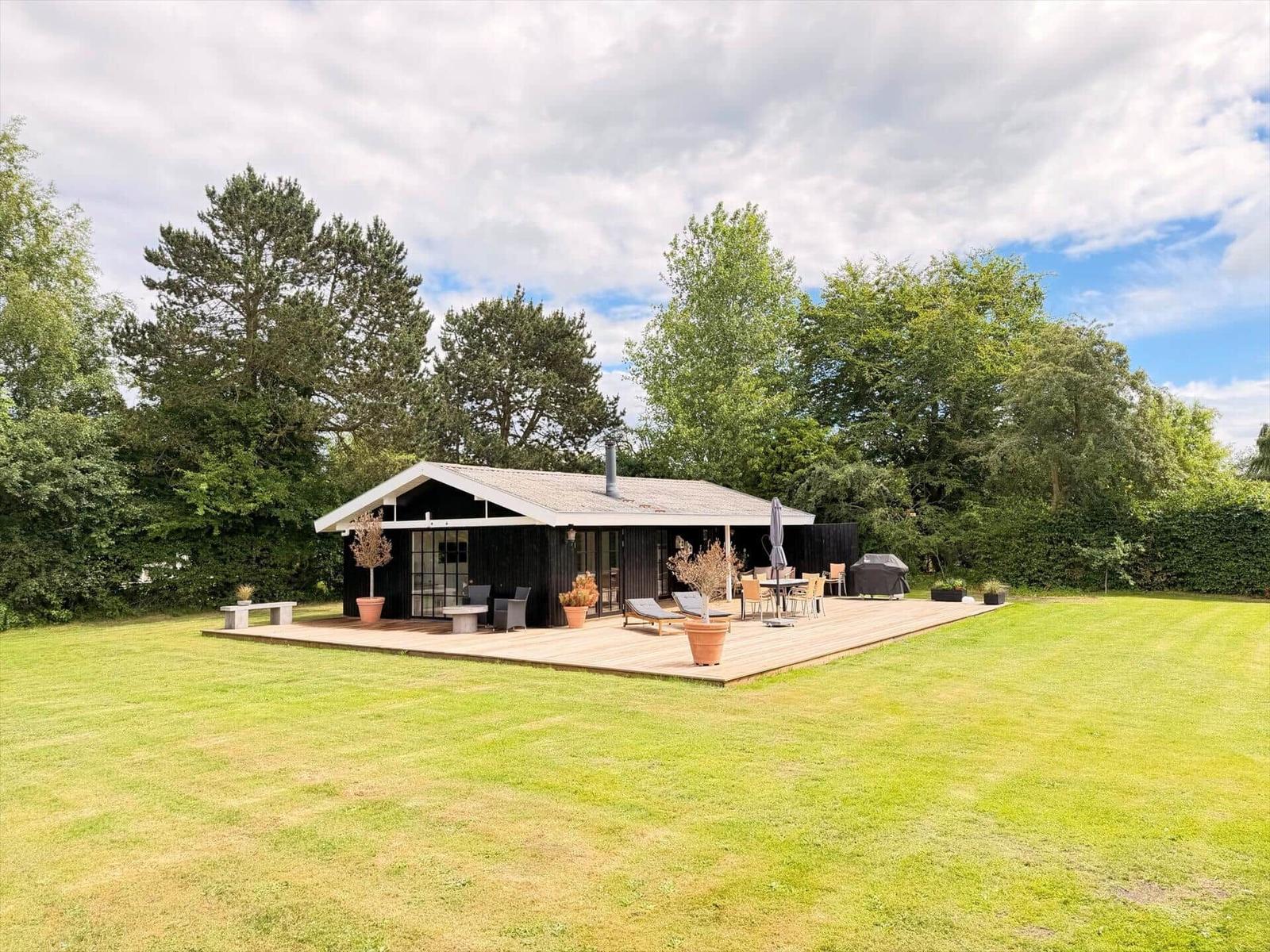Moderne Villa mit Holzterrasse, Garten und Grillplatz. Umgeben von Bäumen und Grün.
