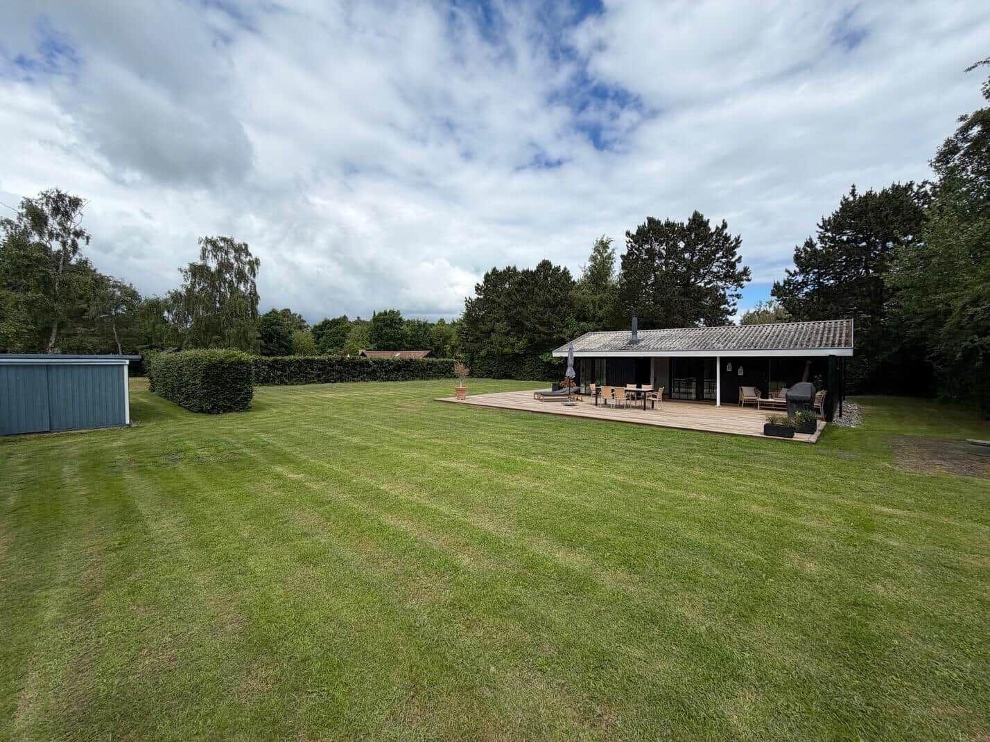 Haus mit Terrasse, Grill und Garten. Umgeben von Bäumen und Rasen.