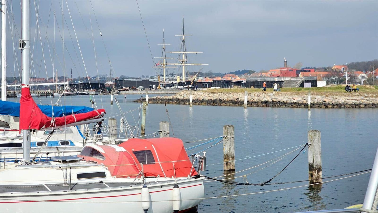 Segelboote liegen im Hafen, im Hintergrund ein historisches Schiff und Gebäude.
