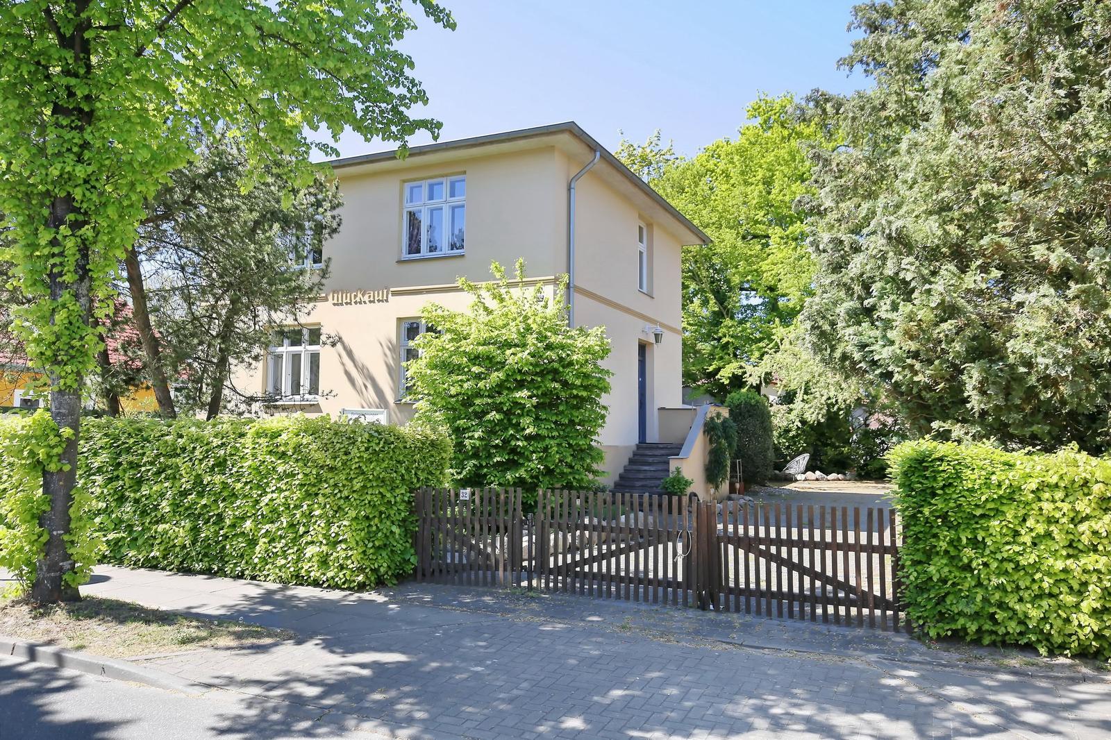 Ein zweistöckiges Haus mit Holztor und grüner Hecke.