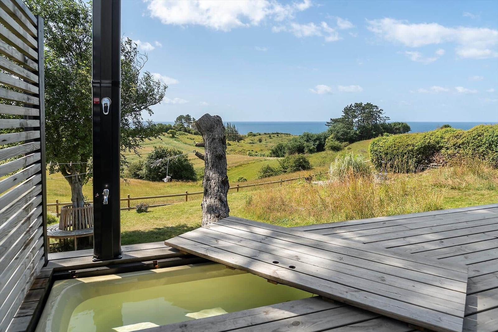 Terrasse mit runden Tisch, Stühlen und Grill. Blick auf Grünflächen und Meer.