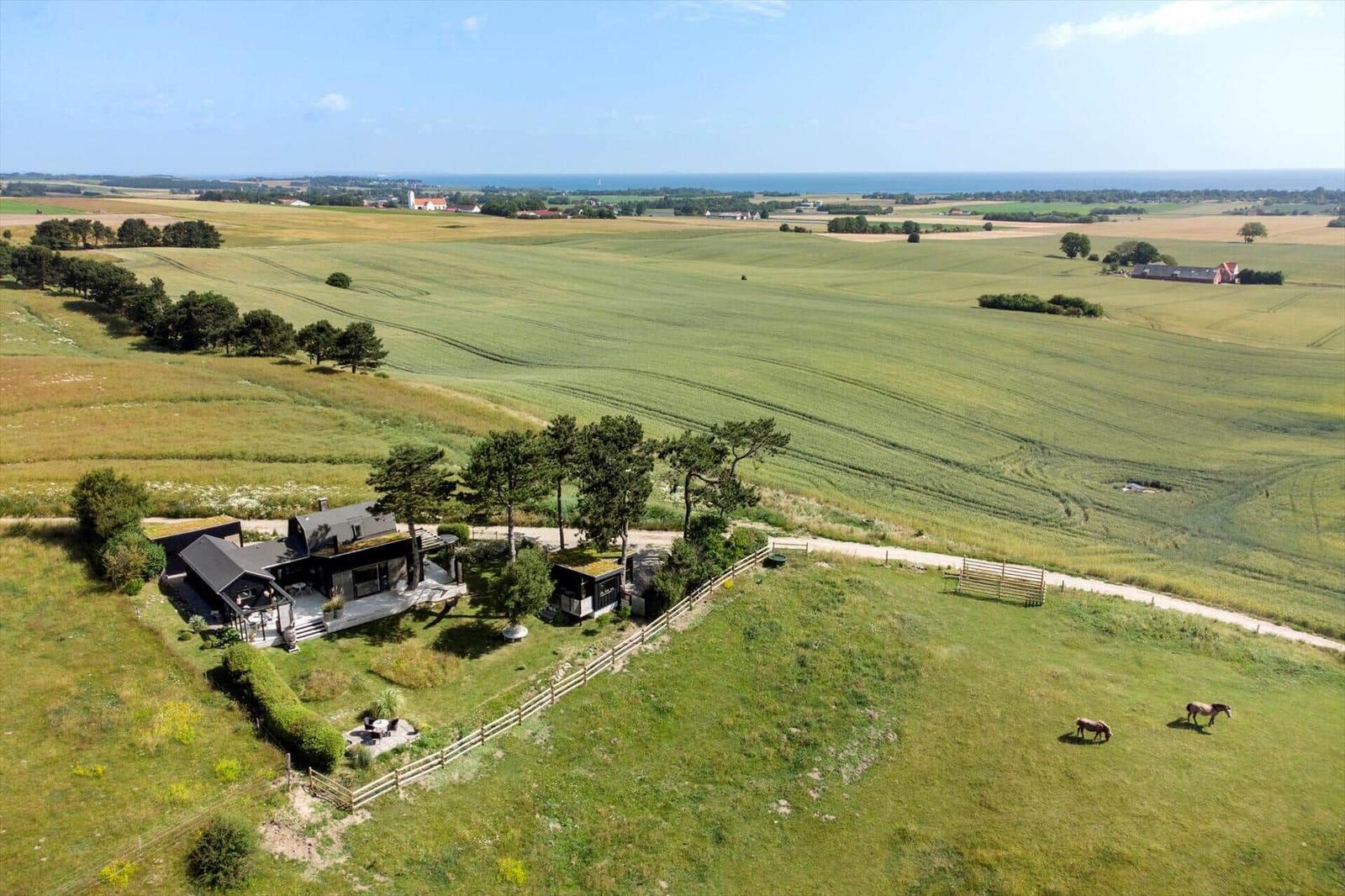 Terrasse mit Sitzgelegenheit und Blick auf grüne Wiesen und Meer.