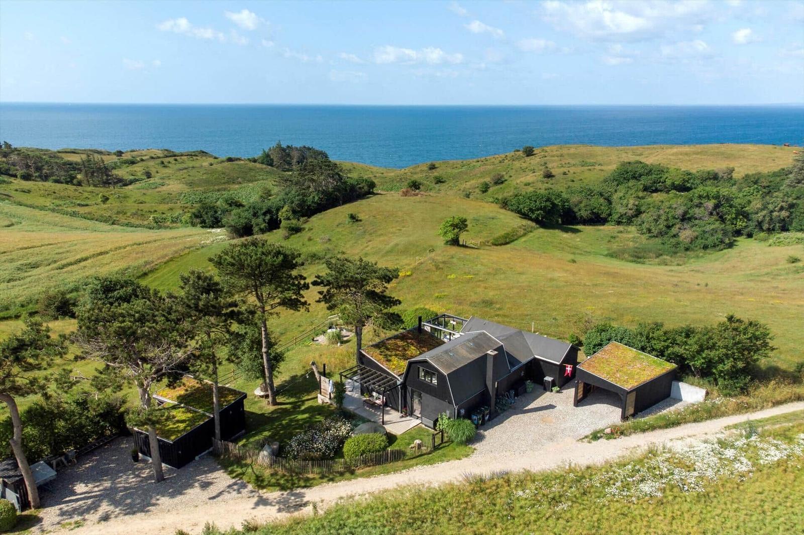 Blick vom Balkon auf grüne Hügel und das Meer unter blauem Himmel.