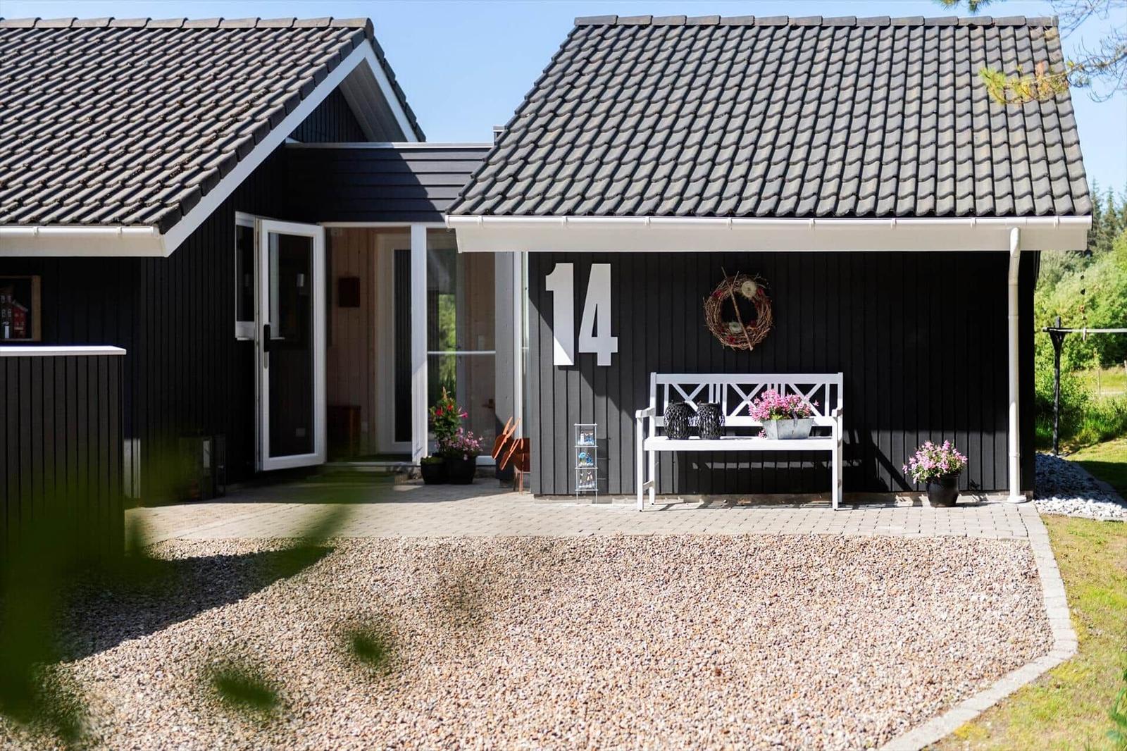 Schwarzes Haus mit weißer Bank und Blumen vor der Tür mit Hausnummer 14.