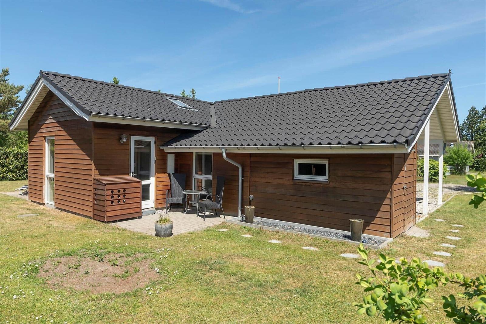 Ein modernes Holzhaus mit Terrasse und Garten. Tisch und Stühle stehen draußen.
