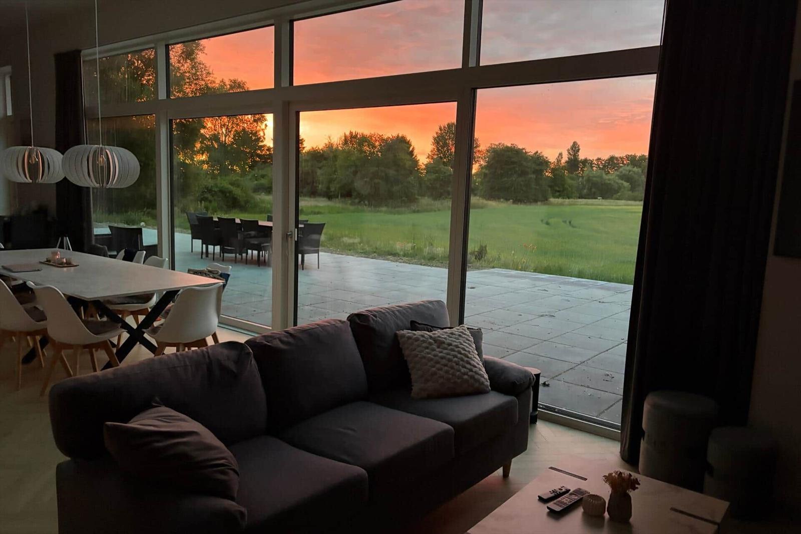 Wohn- und Essbereich mit großem Fensterblick auf Garten und Sonnenuntergang.