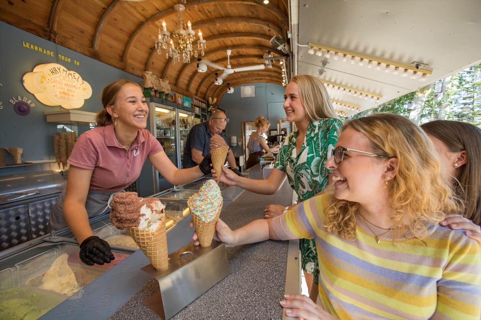 Kunde erhält Eiswaffel an der Theke. Hintergrund zeigt Eisladen mit Kühlschrank und Decke.