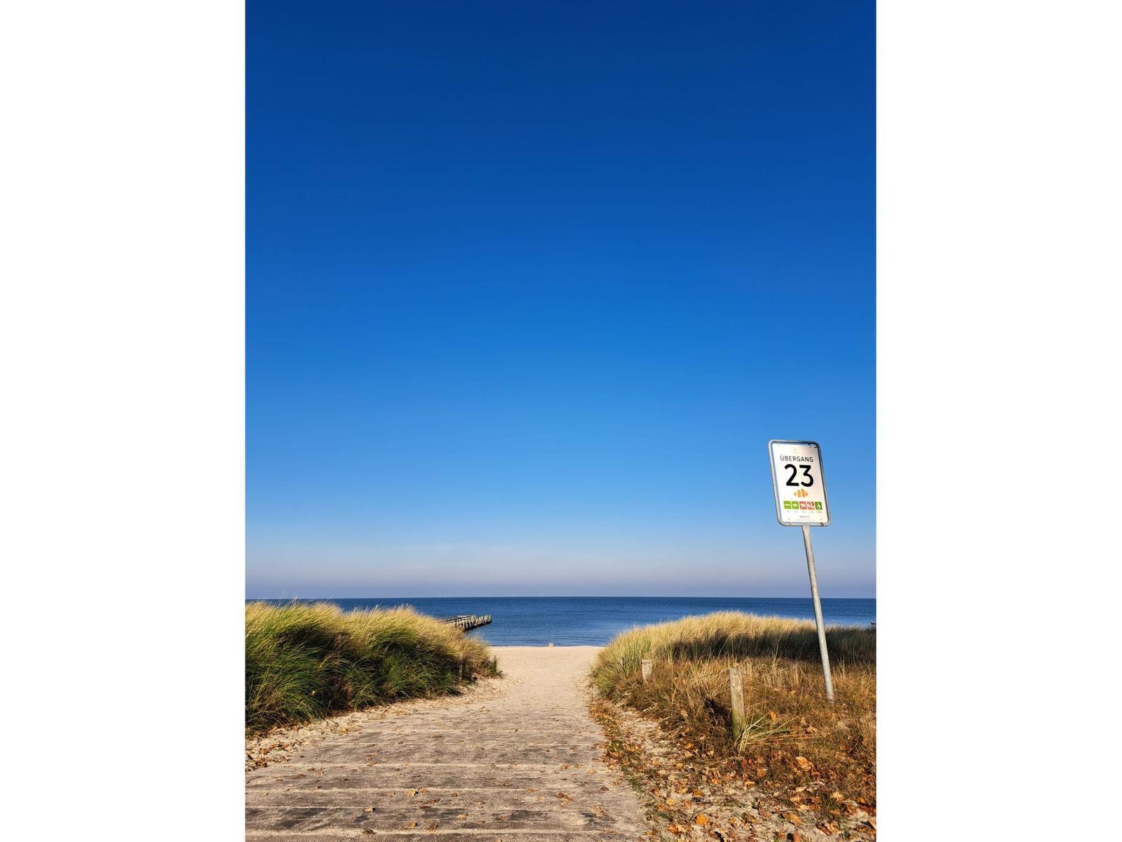 Pfad führt über Dünen zur See. Schild weist auf Übergang 23 hin.