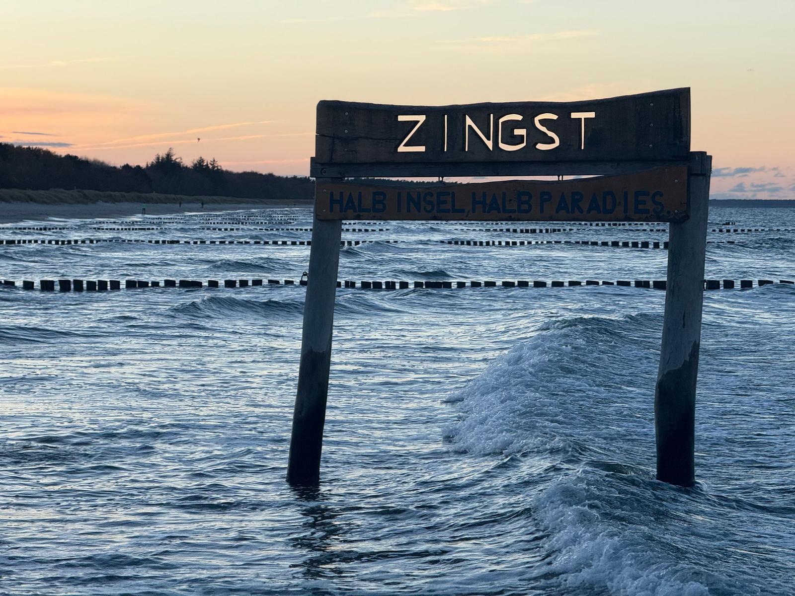 Holzschild im Wasser mit der Aufschrift Zingst und Halbinsel, halb Paradies.