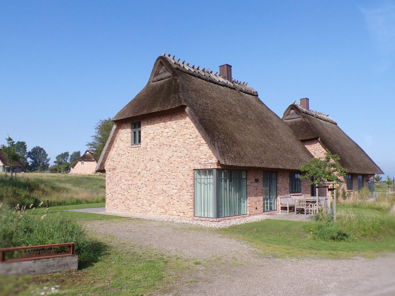 Essbereich mit Holztisch, Stühlen und Fensterbank. Küche mit weißen Schränken und Hängelampen.