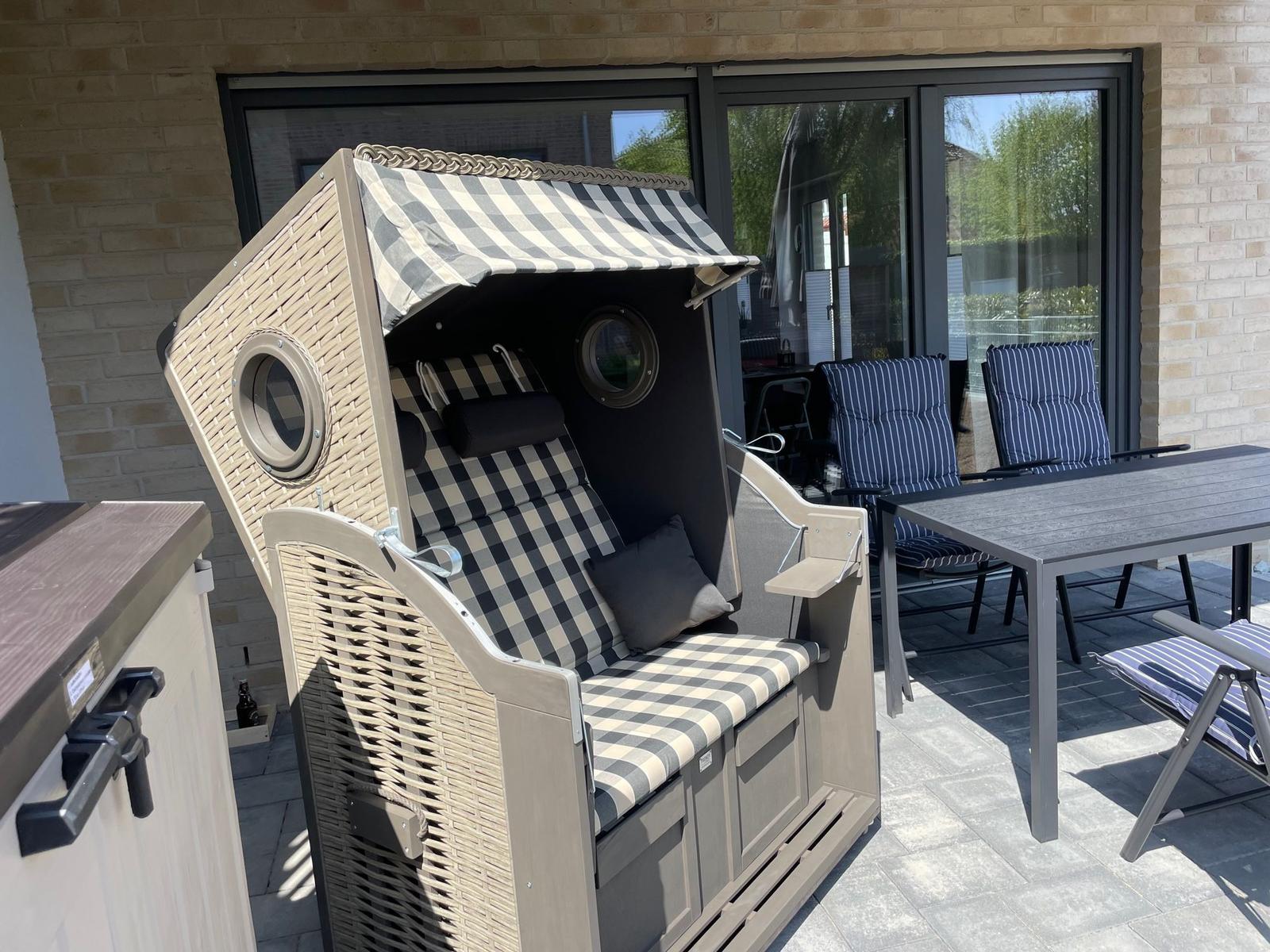 Terrasse mit Strandkorb, Sonnenschirm und Sitzgelegenheiten vor einem Haus.