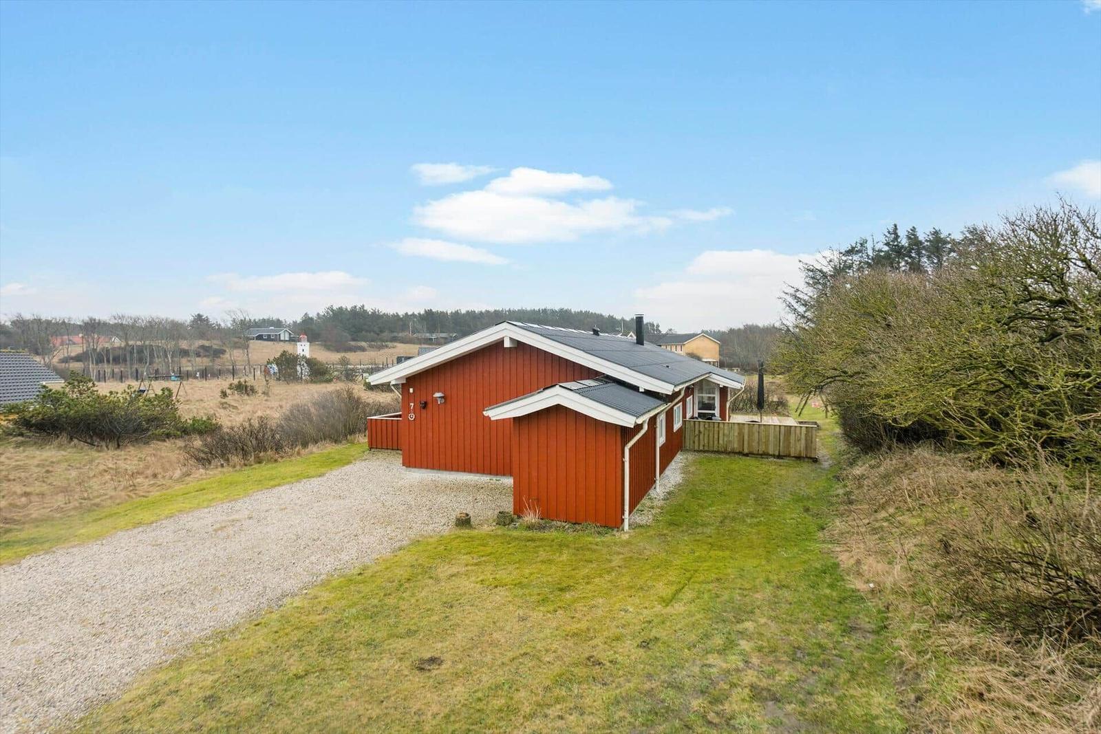Holztisch und Bänke auf grünem Rasen. Im Hintergrund See, Leuchtturm und Gebäude.