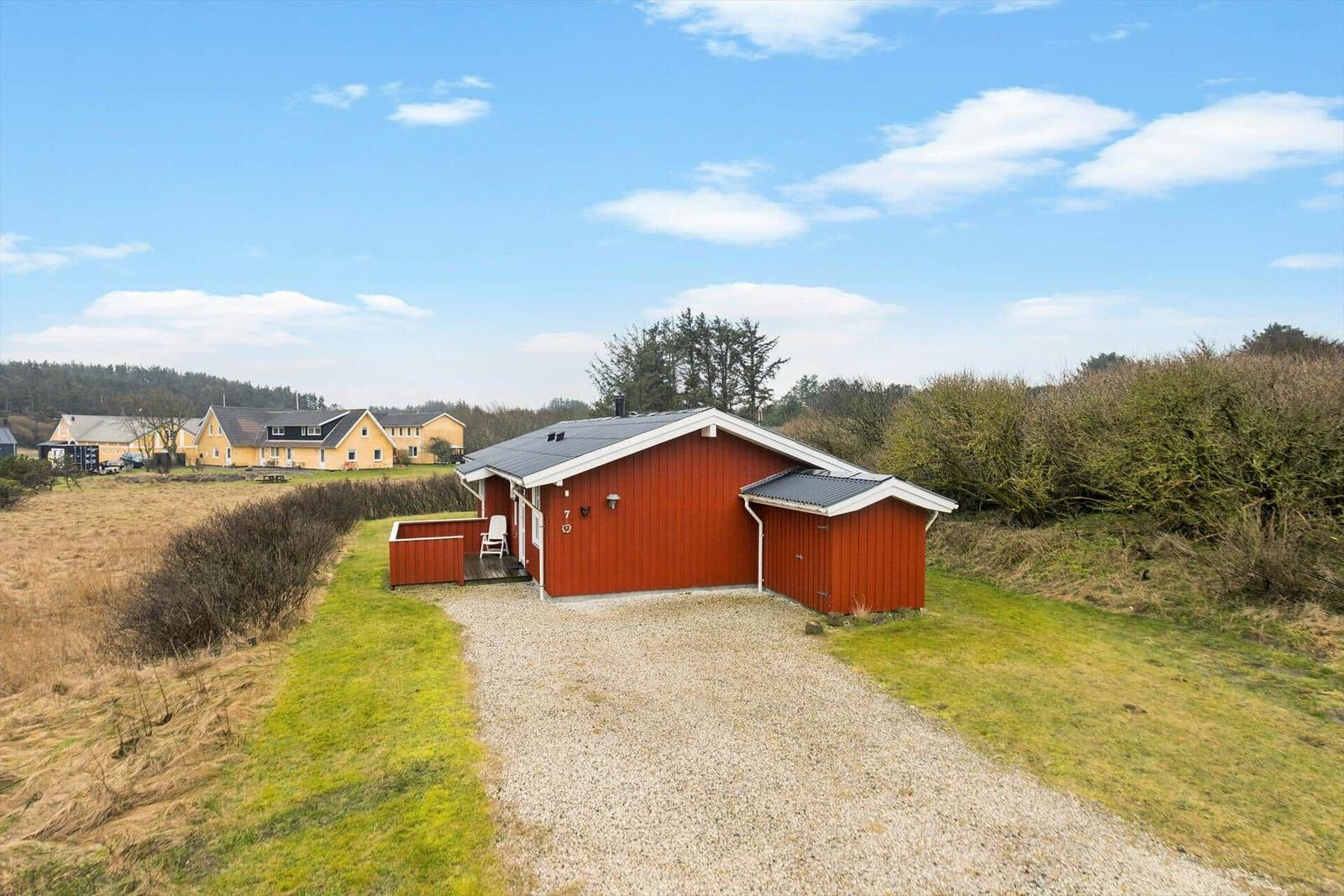 Terrasse mit Tisch und Stühlen vor einem roten Holzhaus mit großen Fenstern.