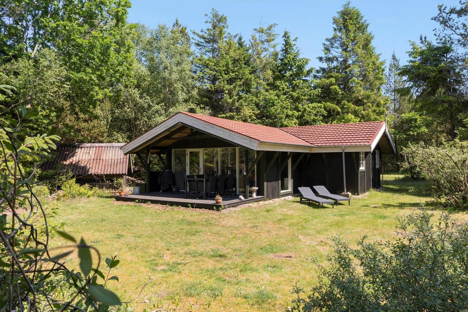 Schlafzimmer mit Bett, Nachttisch und Fenster zur Waldlandschaft.