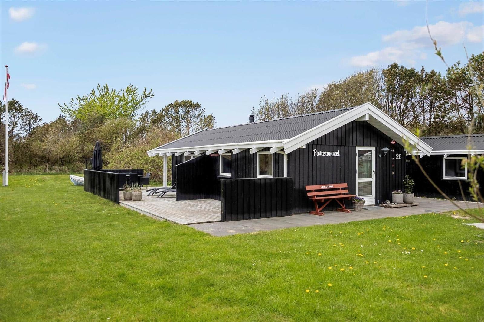 Schwarzes Haus mit weißem Dach, Terrasse mit Liegestühlen und Boot im Garten.