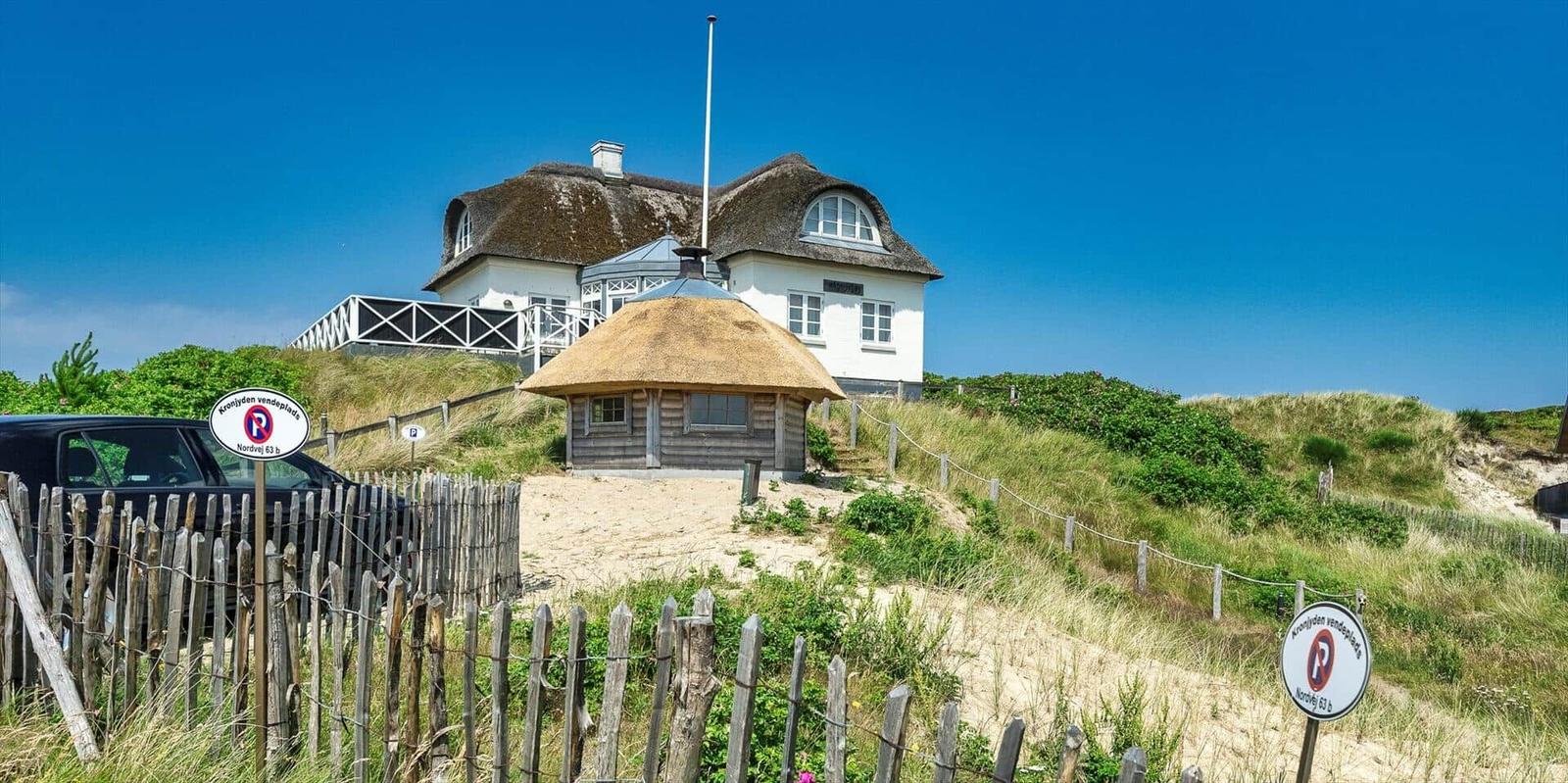 Haus mit Strohdach, Pfad und Blumenhügel unter blauem Himmel.
