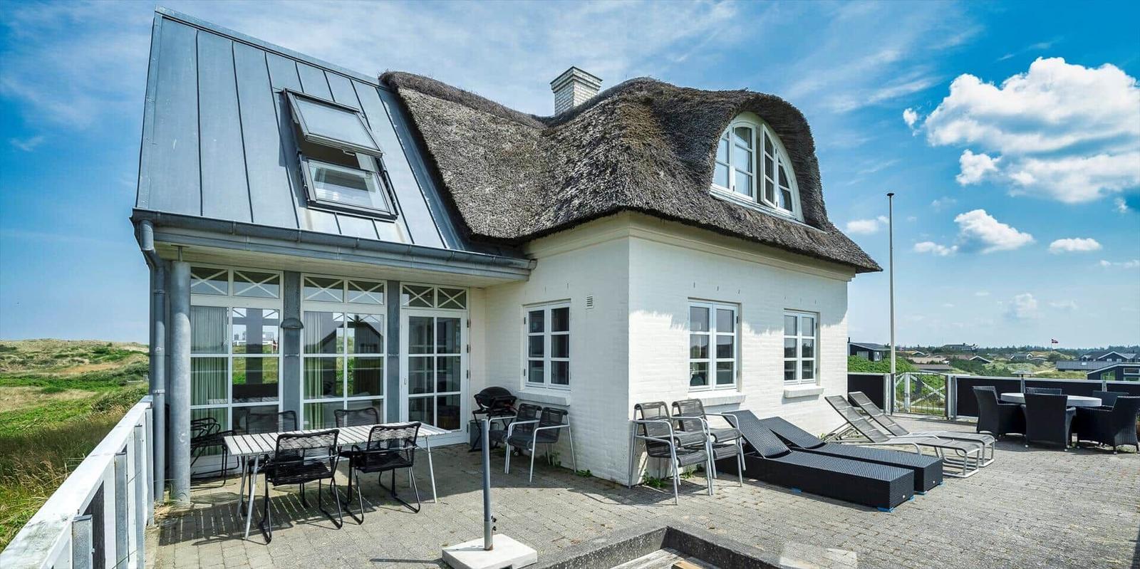 Haus mit Strohdach auf Dünen, Zugang über Steintreppe.