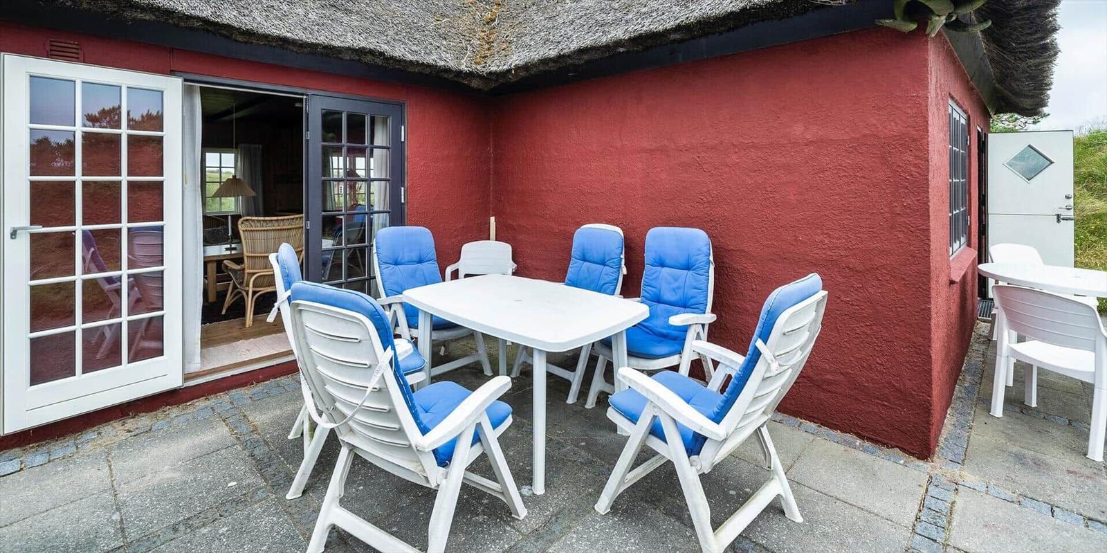 Rotes Häuschen mit Strohdach, Terrasse mit Tisch und Stühlen, Garten und Blick auf die Landschaft.