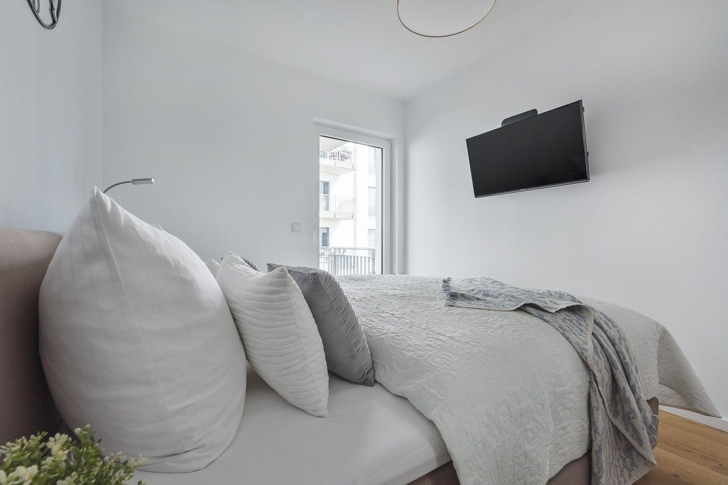 Schlafzimmer mit Bett, Wand-TV und weißen Schränken mit Spiegeltüren.