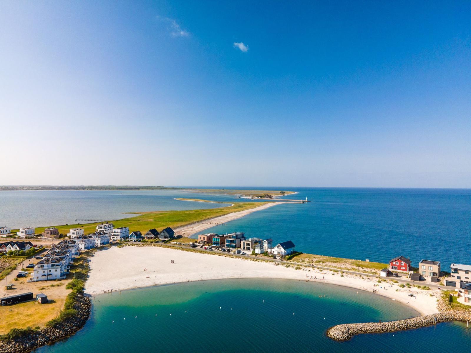 Strandufer mit Häusern und klarem Wasser unter blauem Himmel.