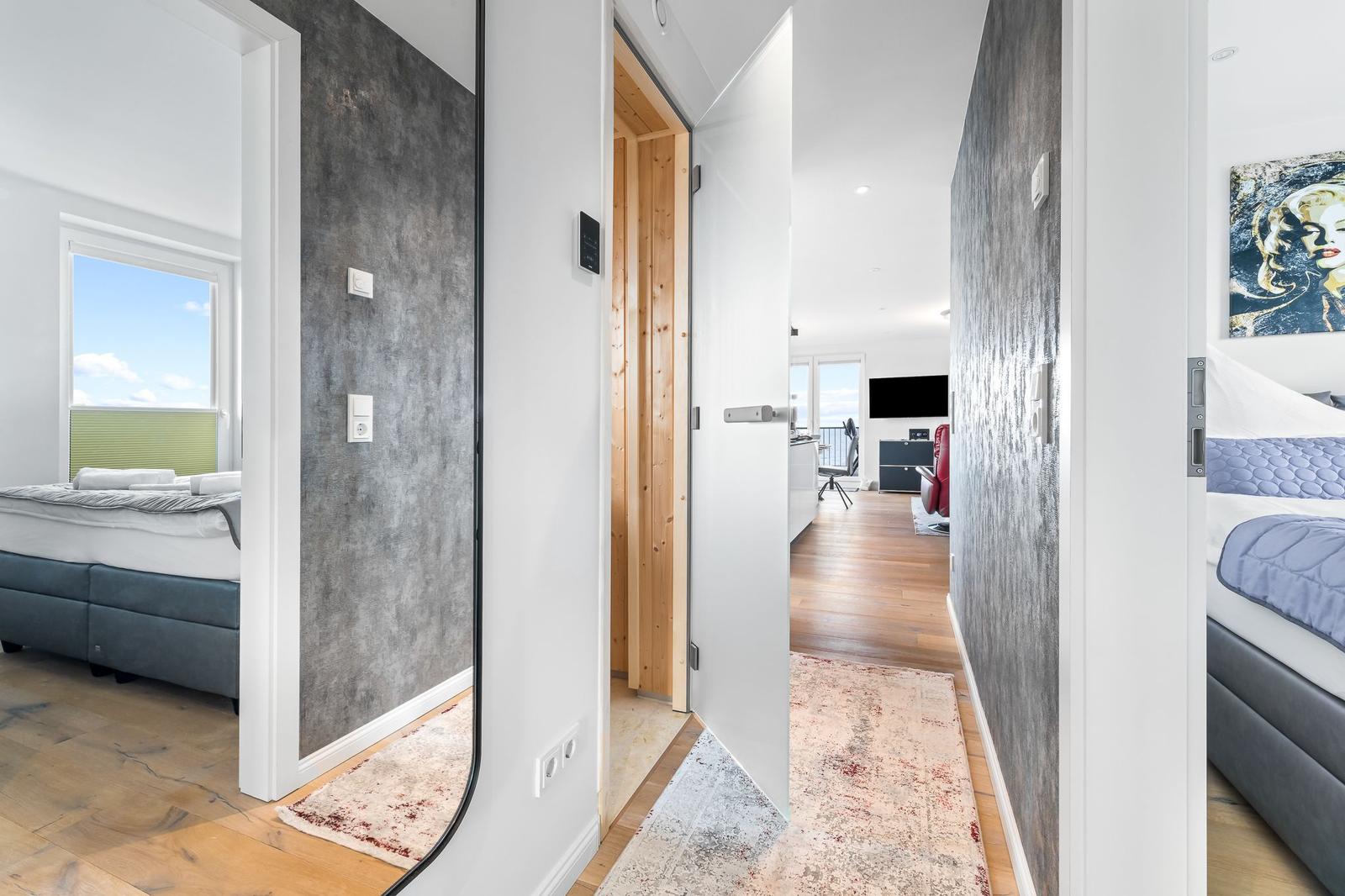 Sauna mit Holzbank, Fenster und Badematten. Spiegel und Tür im Flur.
