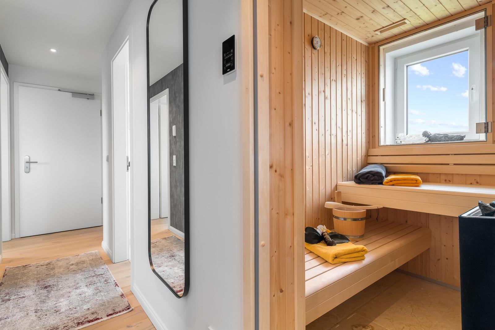 Ein Wohnzimmer mit floraler Couch, grauer Wand und moderner Küchenzeile.