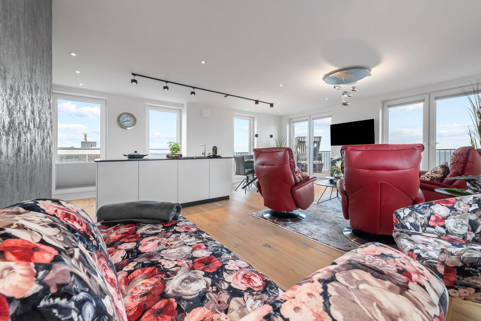 Essbereich mit Tisch und Stühlen, Wohnbereich mit rotem Sofa und Küchenbereich im Hintergrund.