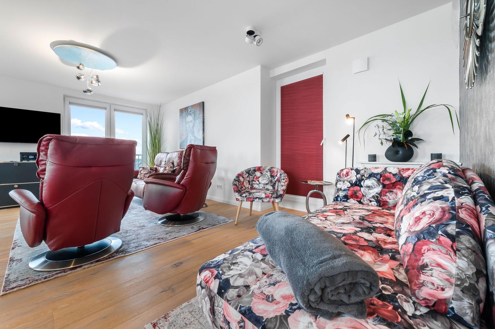 Ein Wohnzimmer mit rotem Sofa, zwei Sesseln, einem runden Tisch und einer Wanddekoration.
