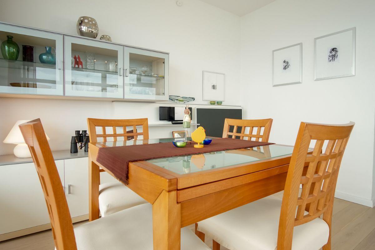 Essbereich mit Tisch, Stühlen und TV-Wand mit Regal und Bildern.