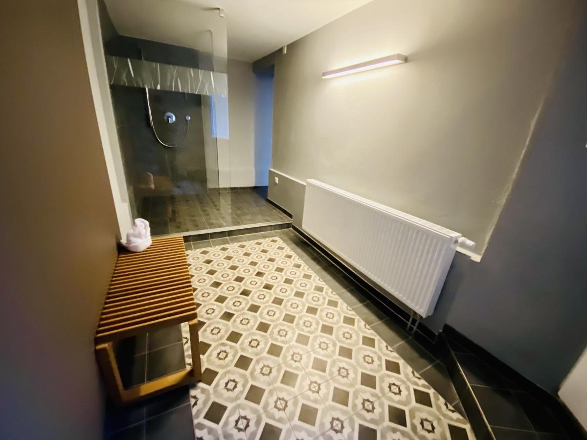 Hinterhof mit Liegestuhl und Tisch mit Stühlen, umgeben von Pflanzen und einer Wand.