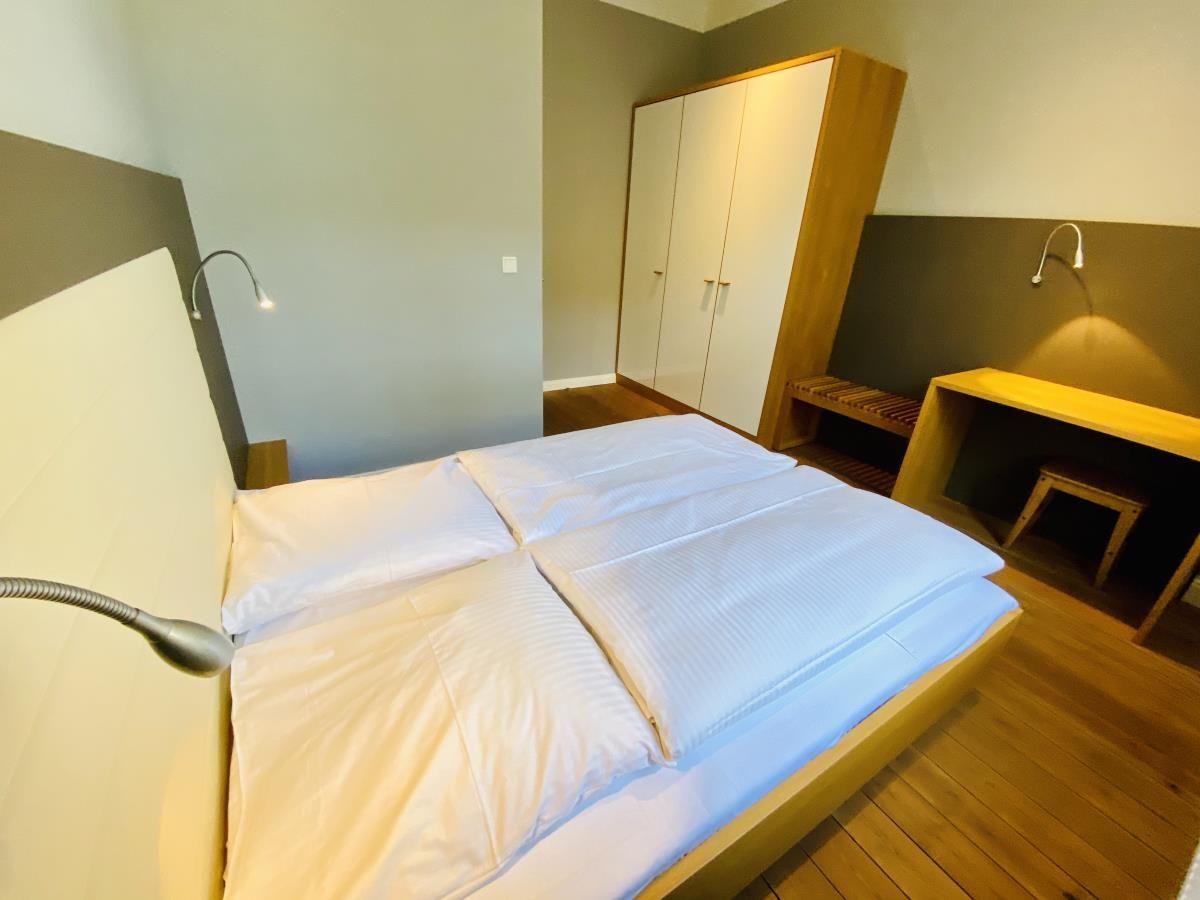 Sauna mit Holzbank, Fenster und Holzwand. Im Hintergrund ist ein Holzbecken mit Löffel zu sehen.