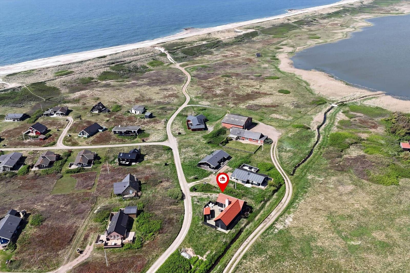 Schwarzes Haus mit rotem Dach auf grünem Gelände. Blick auf Meer und Strand.