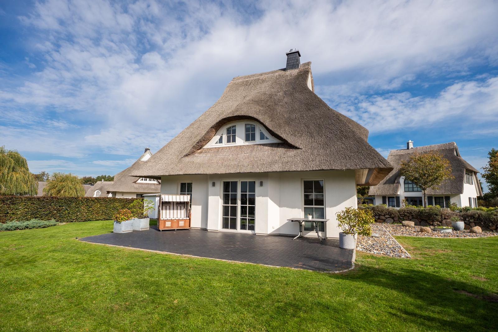 Haus mit strohgedecktem Dach und weißen Wänden. Vorhof mit Steinplatten und Rasen.