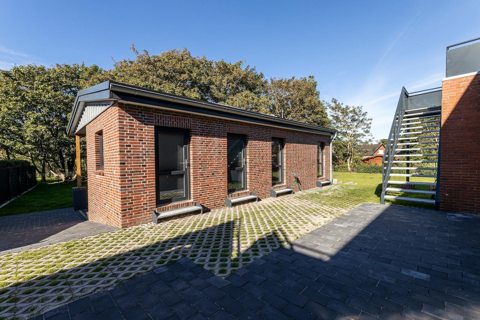 Two e-bikes stand under a roof next to a brick wall on paving stones.