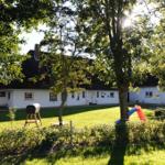 Weiße Villa mit Garten, Spielplatz und Bäumen im Hintergrund.