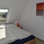 Schlafzimmer mit Dachfenster, Bett und Wandbildern.