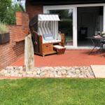 Terrasse mit Liegestuhl, Tisch und Stühlen. Hintergrund: Glasfront und Garten.
