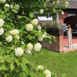 Haus mit Garten, Blumenstrauß und Terrasse mit Sitzgelegenheit.