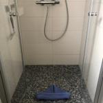 Duschkabine mit Mosaikboden und Handdusche.