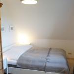 Schlafzimmer mit Bett, Holzschrank und Fenster mit Vorhängen.