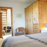 Schlafzimmer mit Bett, Holzschrank und Blick in Wohnbereich mit Sofa.