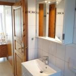 Badezimmer mit Waschbecken, Spiegel und Tür zum angrenzenden Raum.
