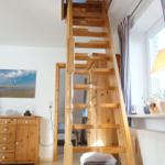 Holztreppe führt zu einer oberen Etage. Im Hintergrund sind Möbel und ein Fenster sichtbar.