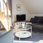 Wohnzimmer mit Sofa, Sessel, Glas-Tisch und Fernseher unter schrägem Dach