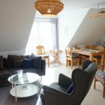 Wohn- und Essbereich mit Sofa, Sessel, Esstisch und Küchenzeile unter Dachschrägen.