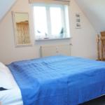 Schlafzimmer mit Dachschrägen, Bett mit blauer Bettdecke, Fenster und Spiegel an der Wand.